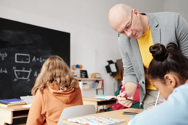 Ein Lehrer hilft einer Schülerin im Klassenraum bei einer Aufgabe